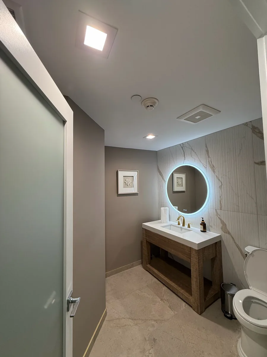 Bathroom with recessed ceiling lights and a round backlit mirror over the vanity