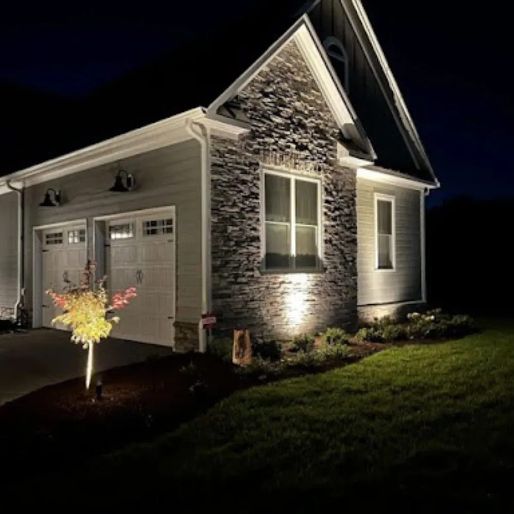 House at night with uplights on the stone facade and a lit tree in the landscaping